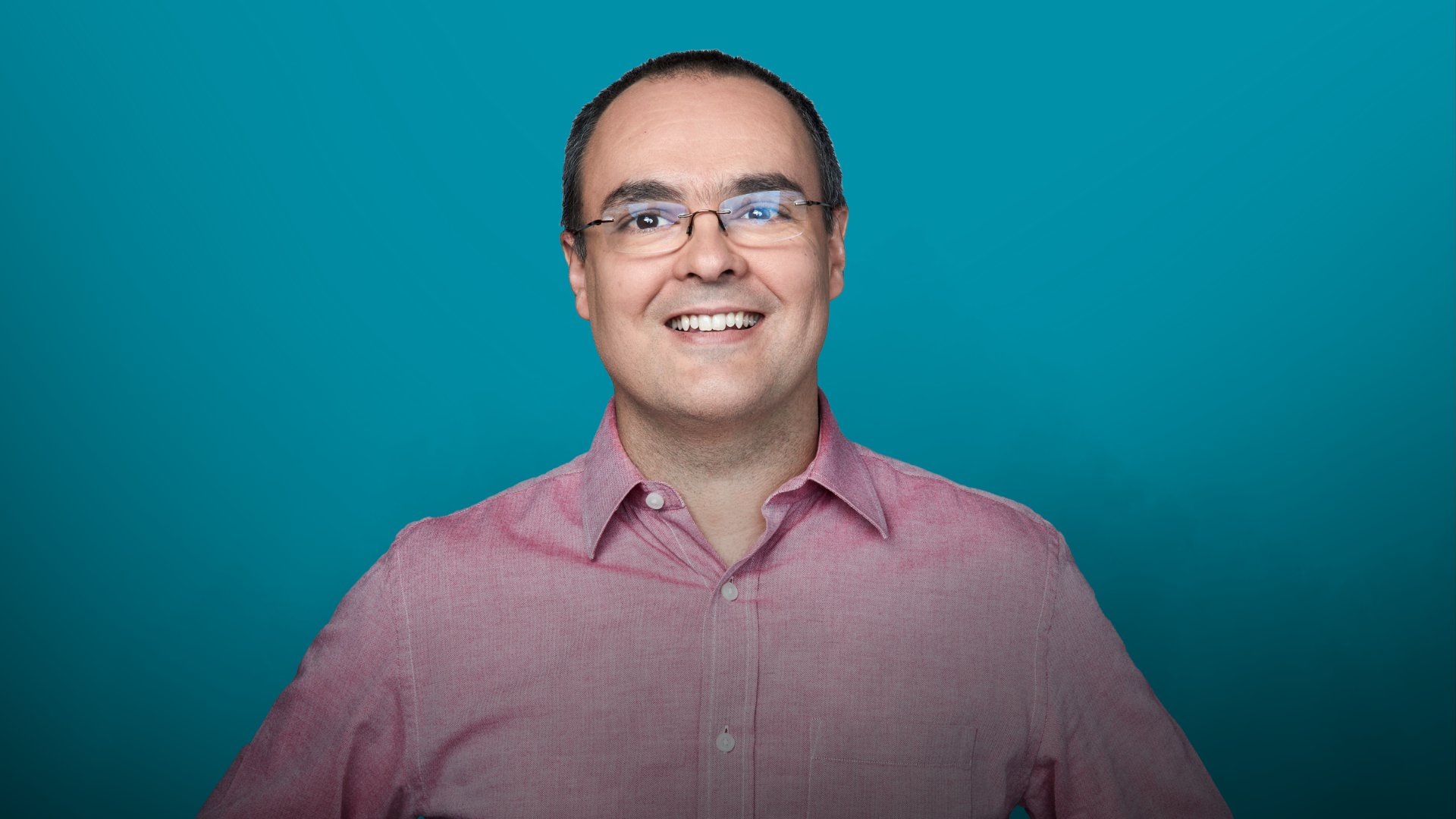 Juan Andrés Muñoz in light red button down shirt on a teal background